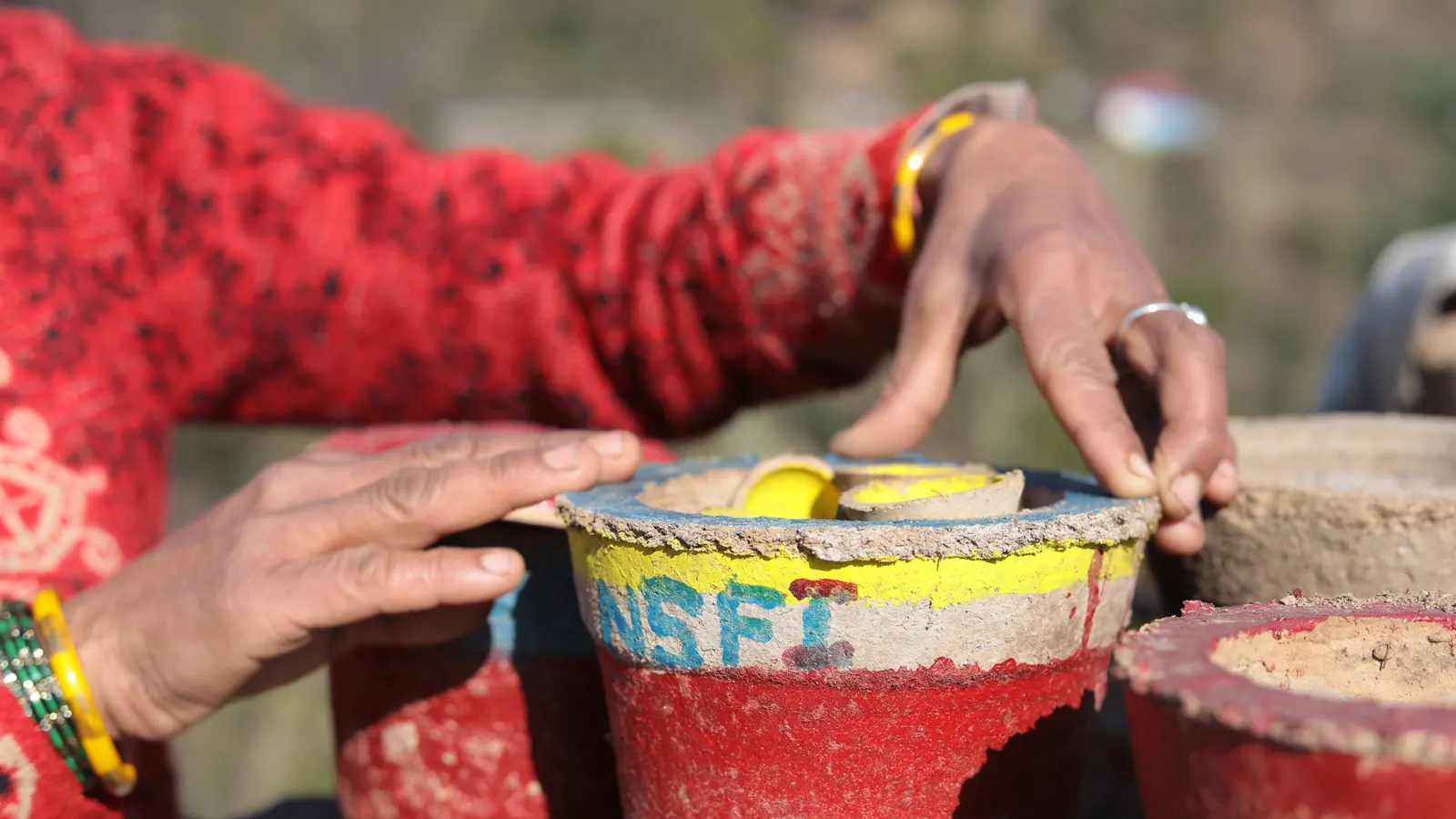 Hands shaping a clay planter marked NSFI during a livelihood training